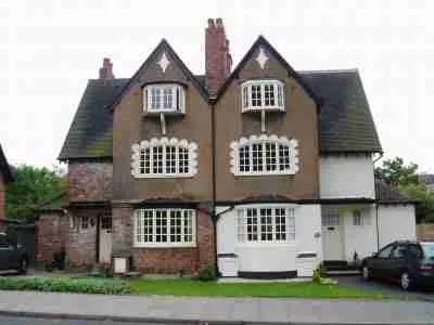 A quaint two-story house with a symmetrical design featuring decorative half-timbering, white stucco walls, and unique window patterns, complete with a tidy front garden and a car parked to the side. homeowner secured loans