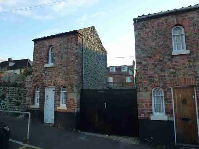 A quaint brick building with an unconventional extension and blocked windows under a clear sky. loans secured against property
