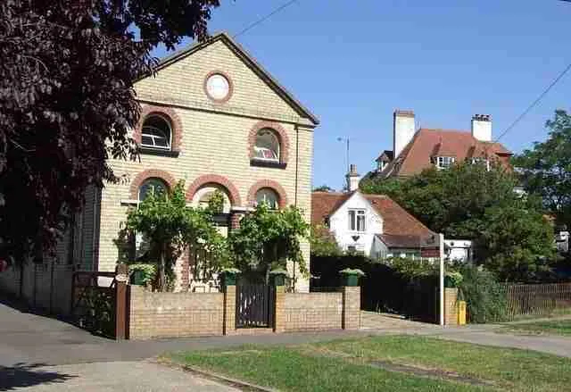 A sunlit suburban street with a charming two-story house featuring brickwork and an arched window, surrounded by lush greenery under a clear blue sky. secured loans poor credit