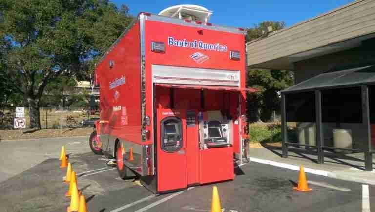 A mobile bank of america atm unit set up in a parking lot, surrounded by orange traffic cones for safety and accessibility. auto bank finance