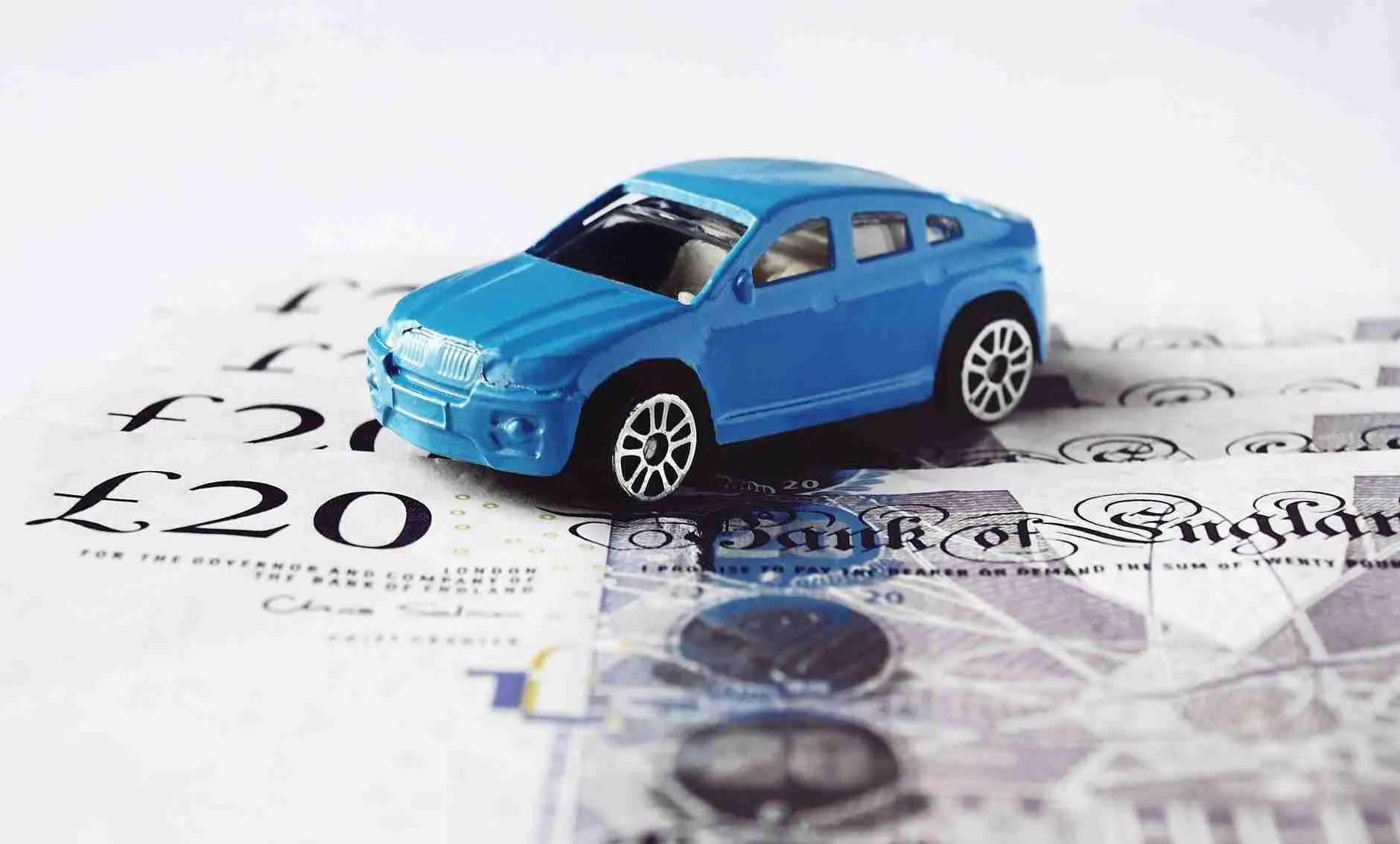 A toy car placed on top of a spread of british 20 pound notes, symbolizing the concept of the cost of vehicles or savings for a car.