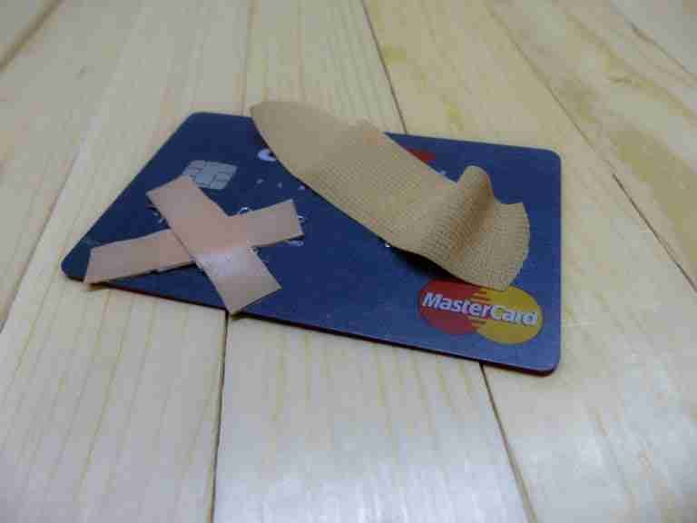 A damaged credit card with adhesive bandages applied to it on a wooden surface, symbolizing a financial setback or the concept of repairing credit.