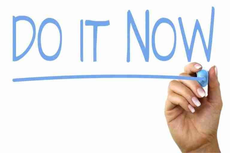 A hand holding a marker after writing the motivational phrase "do it now" in capital letters on a white background.