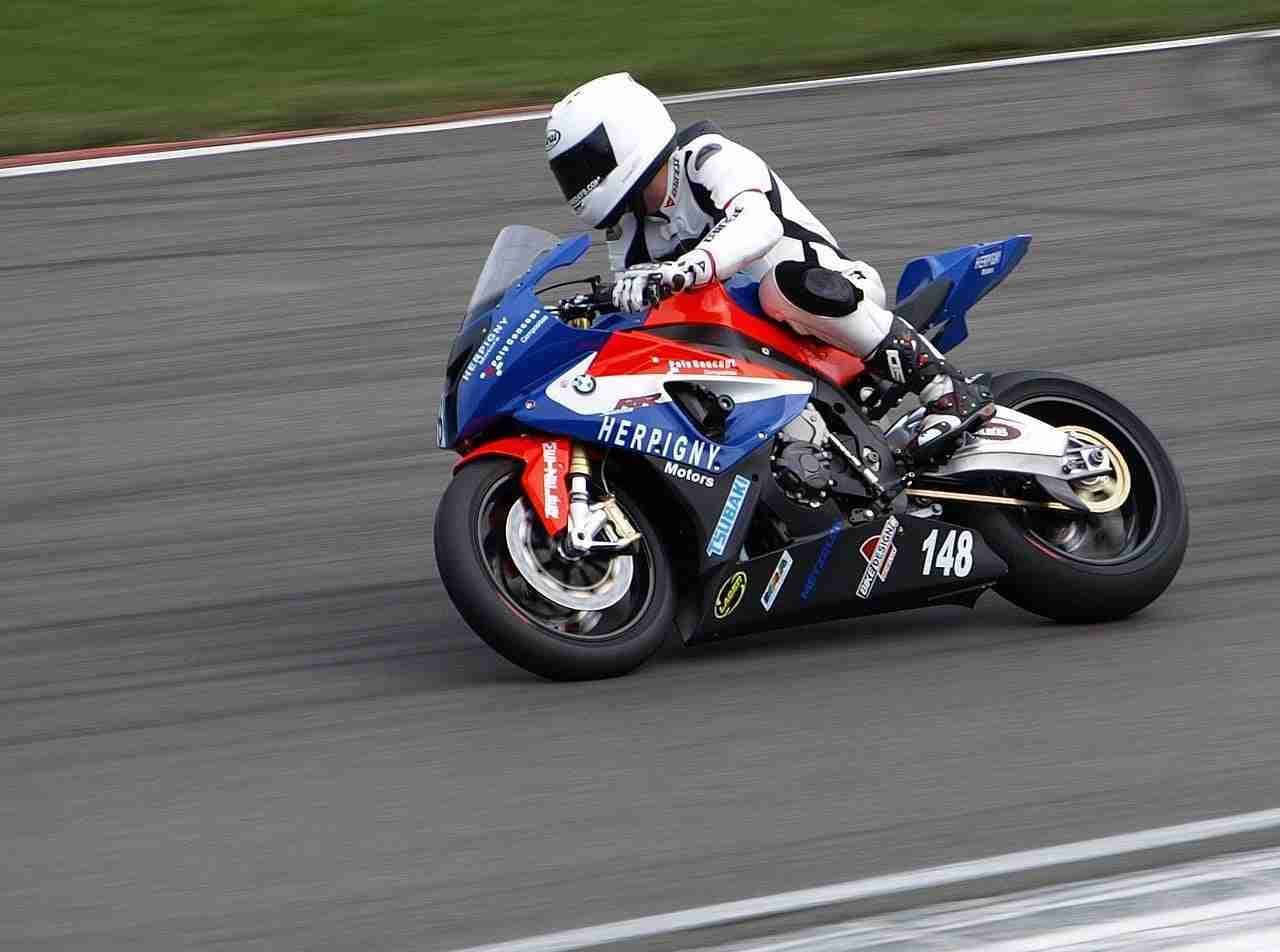 A motorcycle racer leans into a turn on a racetrack, focused and fast, showcasing skill and speed.