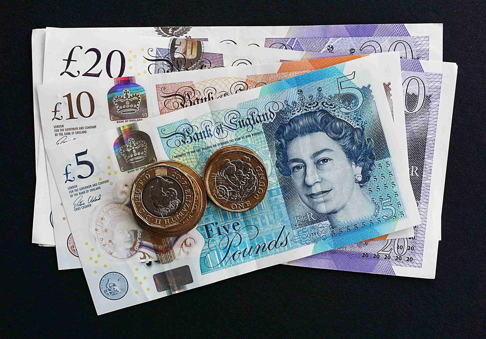 A collection of british currency, including various banknotes and coins, arranged on a dark surface. small loans.