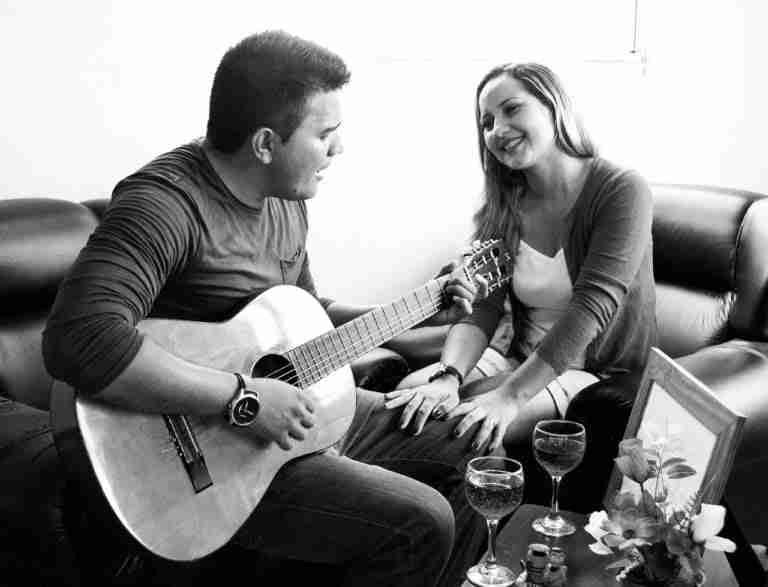 A moment of musical connection: a man serenades a smiling woman with an acoustic guitar as they enjoy a cozy atmosphere with glasses of wine on the table.