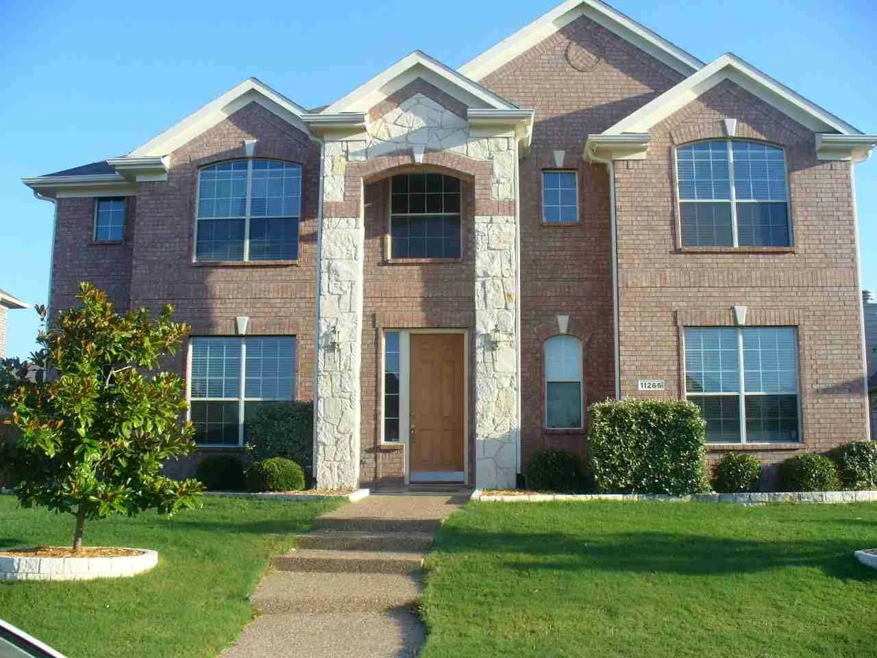 A two-story suburban brick home with a prominent entrance and symmetric windows under a clear blue sky. homeowner loan.