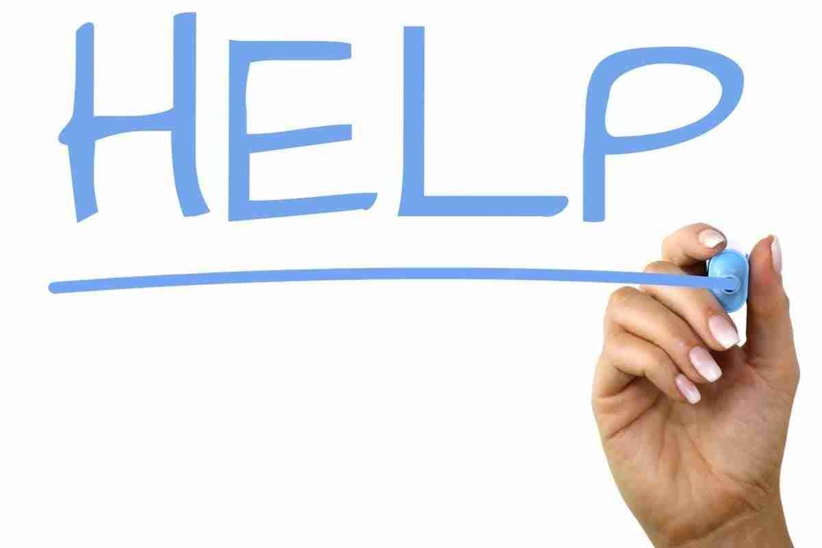 A hand writing the word "help" in capital letters with a blue marker on a clear surface, conveying a message of assistance or support needed.