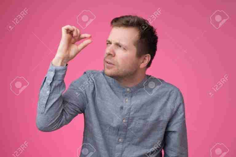 A man holding up his fingers close to each other, squinting as if judging or measuring something very small, with a skeptical expression on a pink background.