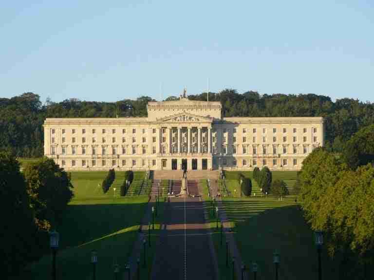 Majestic historic building of stormont northern ireland with a classical façade, neatly manicured lawns, and a long tree-lined approach, basked in sunlight. car finance ni