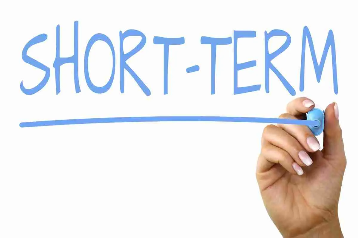 Hand writing the words "short-term" on a clear surface with a blue marker.