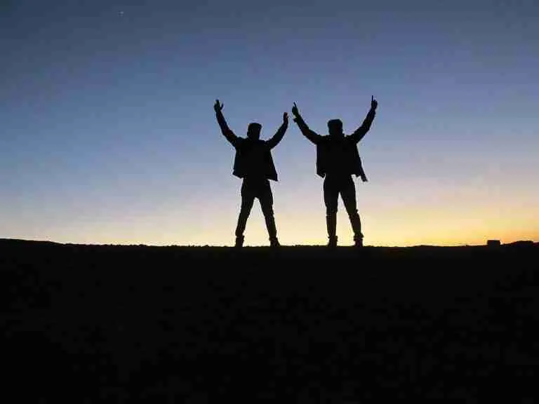 Two silhouetted figures with raised arms against a dusky sky, standing on a horizon line. amigo guarantor loans