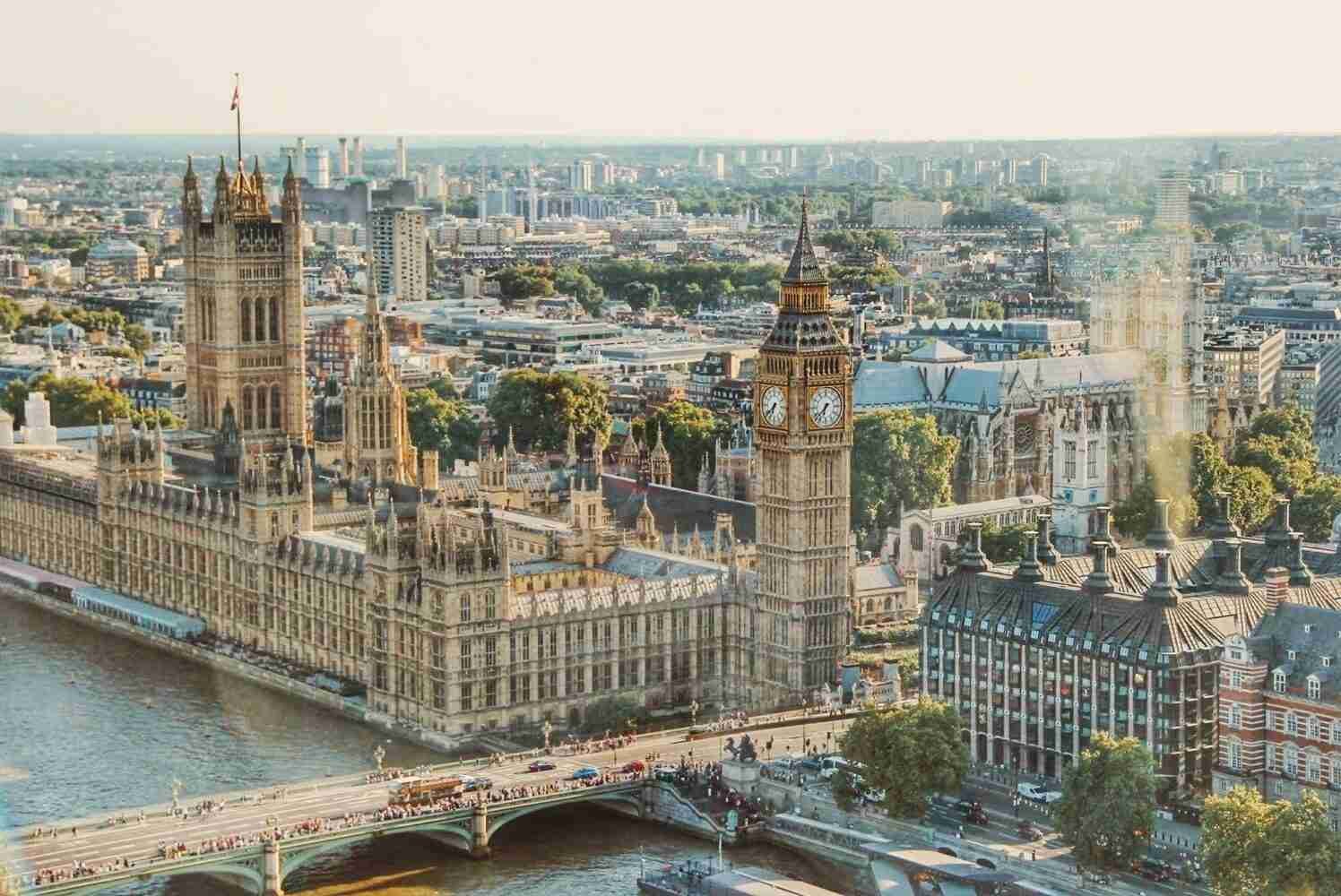 Aerial view of the Palace of Westminster with the iconic Big Ben clock tower and Westminster bridge over the River Thames in London during daylight.