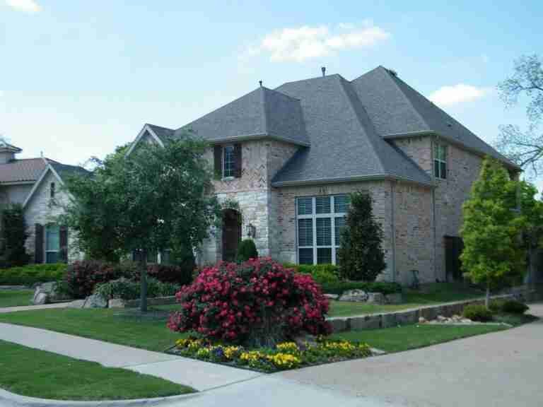 A two-story brick house with a steeply pitched roof, landscaped garden with flowering shrubs, and a well-manicured lawn on a clear day. homeowner loans bad credit