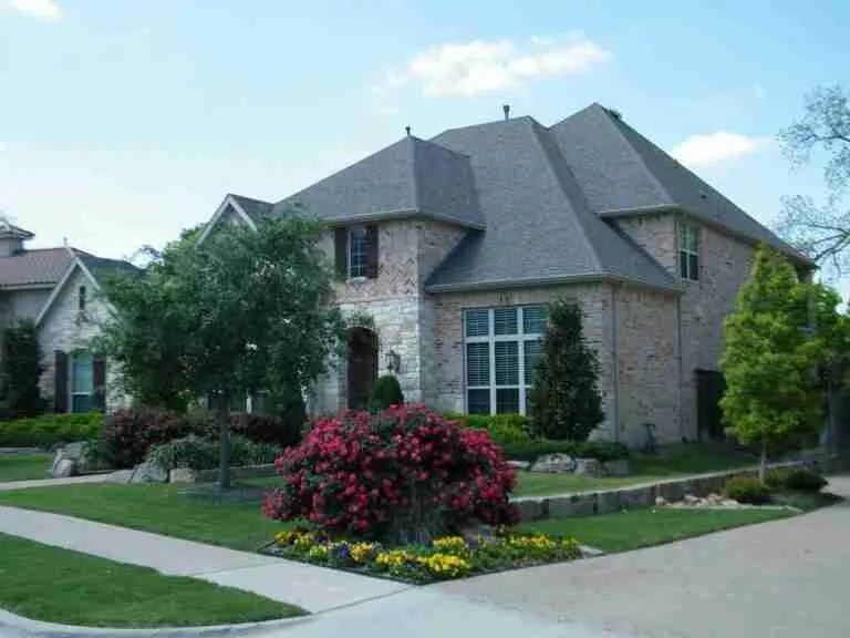 A two-story brick house with a steeply pitched roof, landscaped garden with flowering shrubs, and a well-manicured lawn on a clear day. homeowner loans bad credit