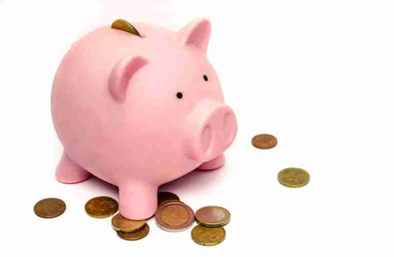 A pink piggy bank with a coin slot on top surrounded by various scattered coins, against a white background.