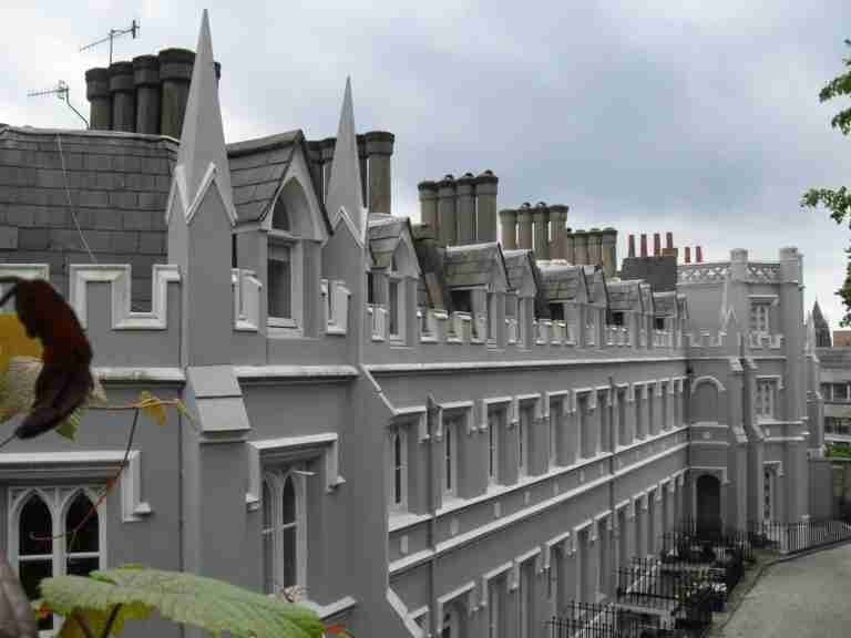 A row of traditional Victorian houses with distinct architectural detailing, including sharp gables and multiple chimneys, under a cloudy sky. Some foliage is visible in the foreground. secured homeowner loans