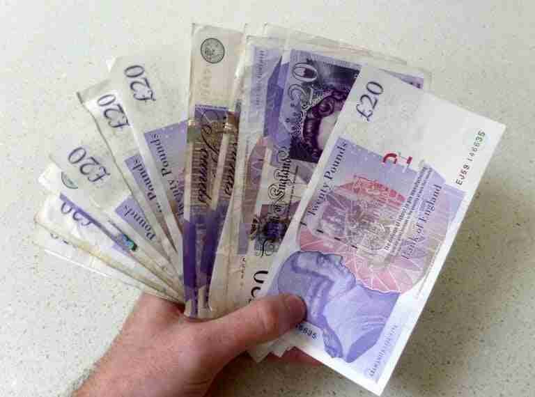 A person's hand holding multiple twenty-pound sterling banknotes against a white background. Borrow 200 Pounds