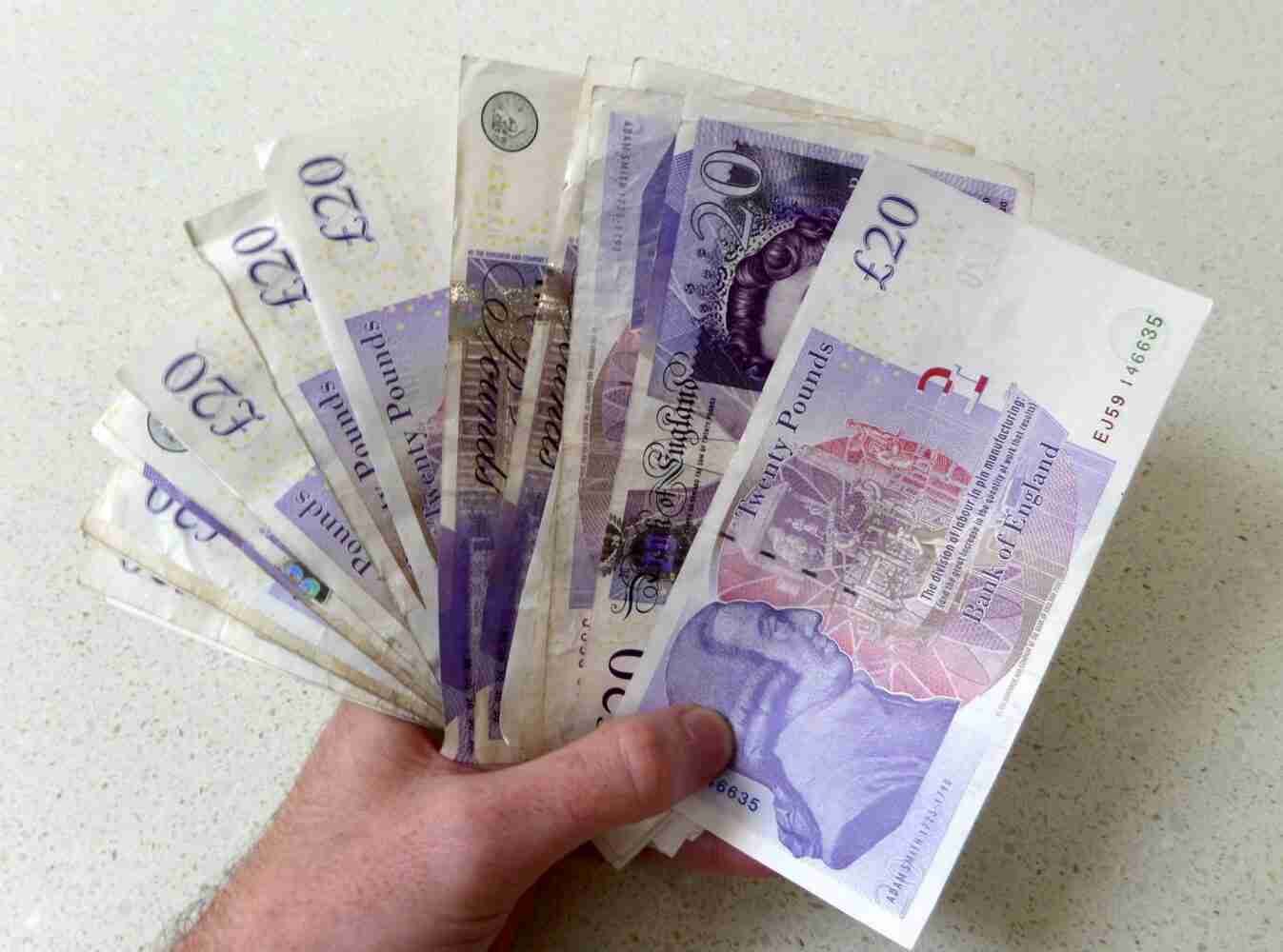 Cash Loans ASAP With New Lenders A hand holding multiple British pound banknotes in denominations of £20 and £5 on a light surface. cash loans
