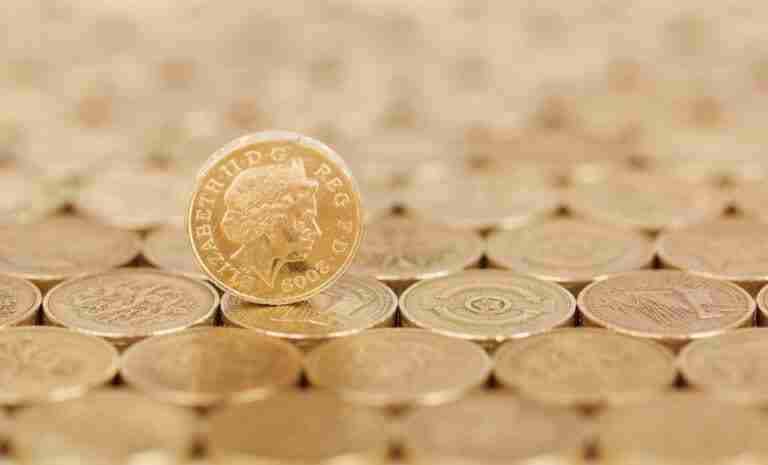 Alt text: A close-up of numerous stacked coins with one coin standing upright, prominently in focus against a blurred background of more coins.