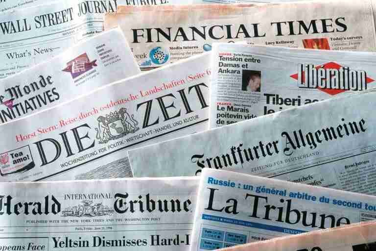 A collection of various international newspapers spread out, displaying parts of their front pages with headlines visible. Some of the newspaper titles shown include "The Wall Street Journal," "Financial Times," "Le Monde," "Die Zeit," "Libération," "Frankfurter Allgemeine," and "International Herald Tribune."