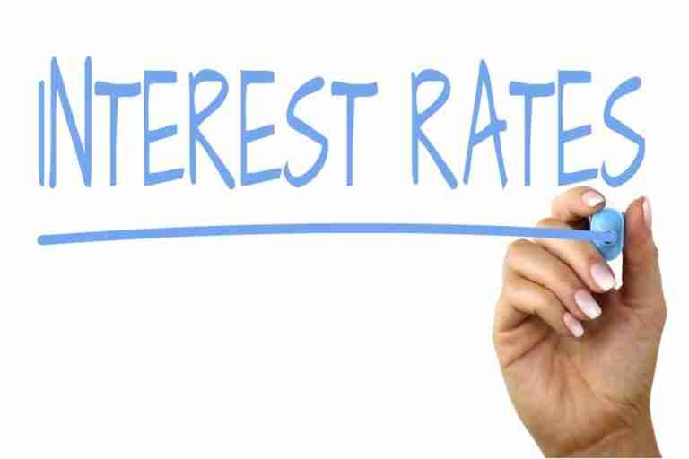 Hand writing "INTEREST RATES" with a blue marker on a clear, white background.