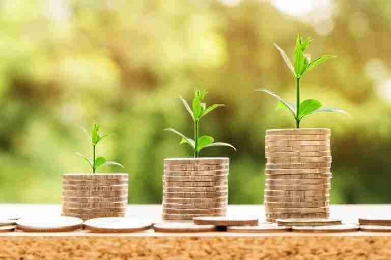 Three ascending stacks of coins with young green plants growing on top, symbolizing financial growth or investment, on a blurred natural background.