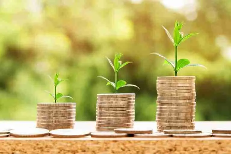 Three ascending stacks of coins with young green plants growing on top, symbolizing financial growth or investment, on a blurred natural background.