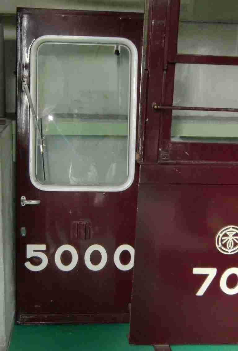 A close-up of a partially open train carriage door with the number "5000" on it, adjacent to another section with the number "7000" and a circular emblem.