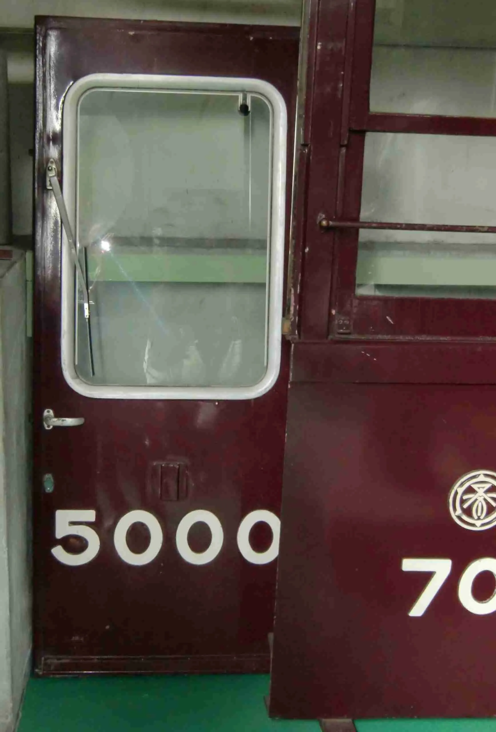 A close-up of a partially open train carriage door with the number "5000" on it, adjacent to another section with the number "7000" and a circular emblem.