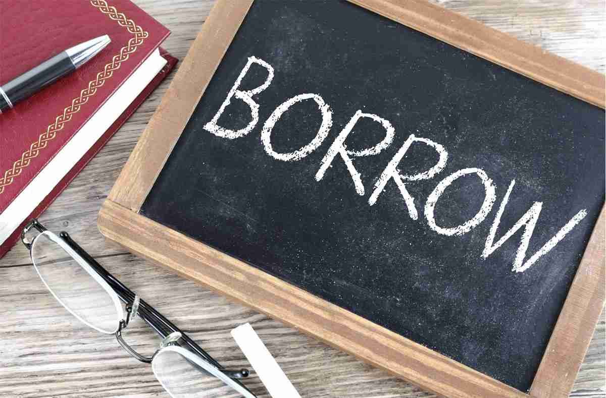 A chalkboard with the word "BORROW" written on it, accompanied by a pair of glasses, a white chalk piece, and a closed book with a pen on top, all resting on a wooden surface. borrow money online