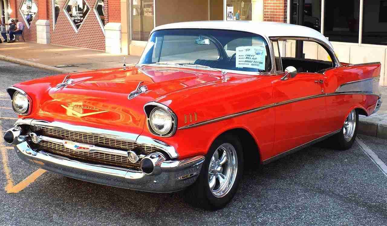 A classic red 1957 Chevrolet Bel Air parked on the street with a for-sale sign in the side window. car finance company