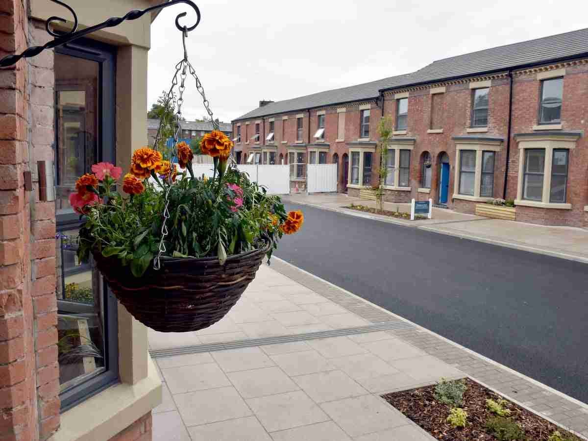 A hanging flower basket in the foreground with vibrant flowers, in front of a residential street with a row of terraced houses. secured loan bad credit