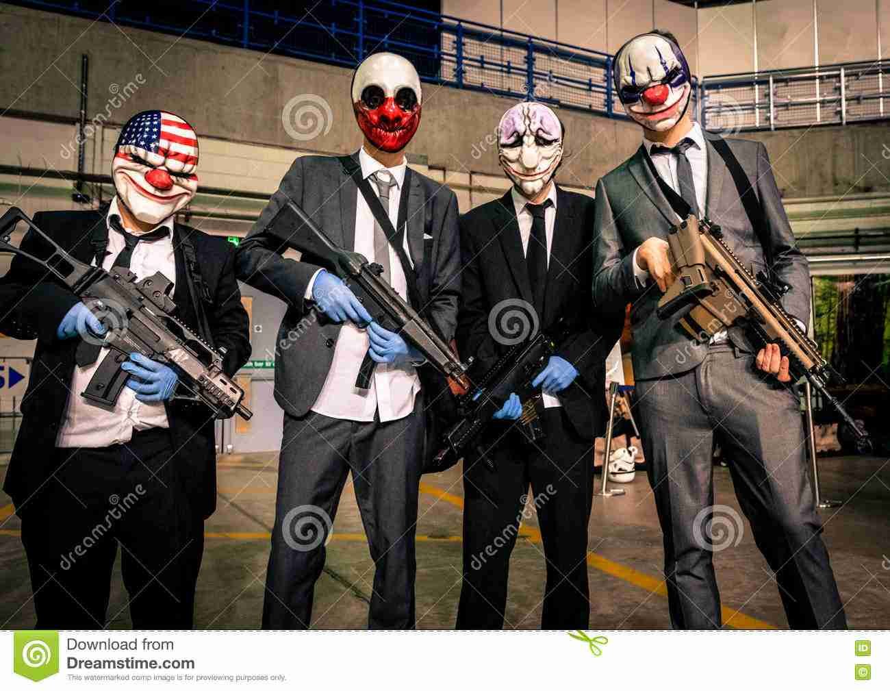 Four people in suits wearing clown masks and holding rifles indoors, with a watermark from Dreamstime from the pay day film. pay day uk.