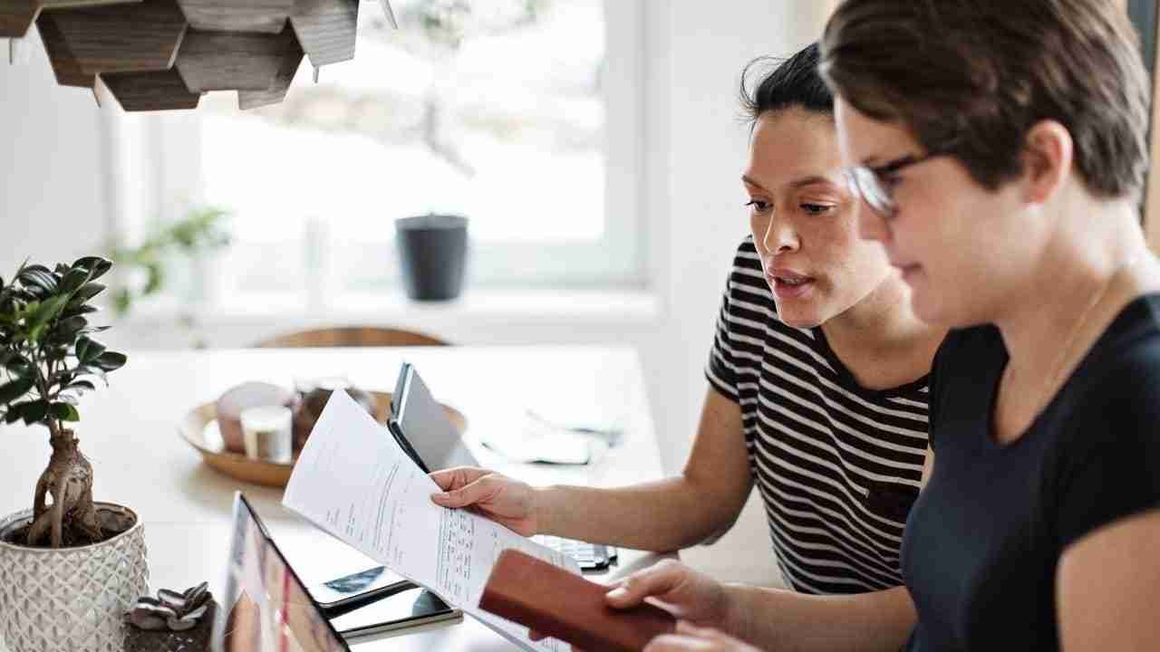 Two individuals are working together at a table with papers and a tablet, in a room with modern decor and a plant on the table. payday loans bad credit direct lender.