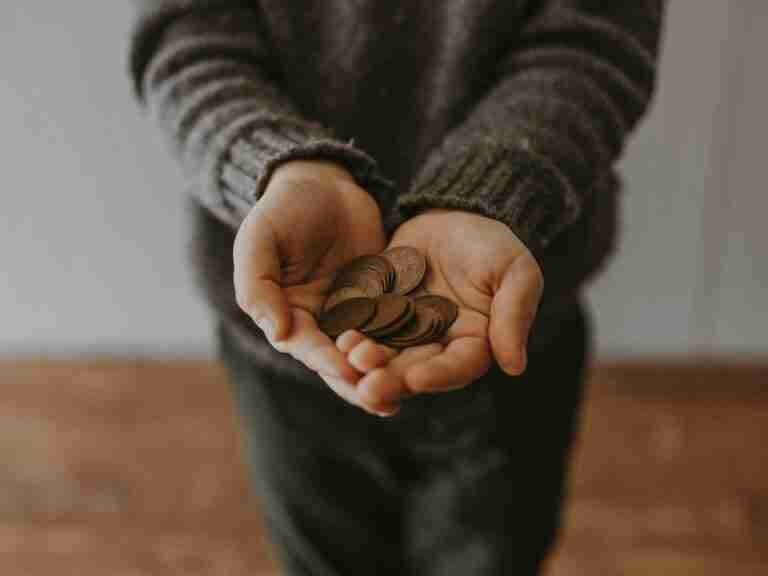 A person in a dark sweater holding a handful of coins extended towards the viewer. £100 pound loans in the UK