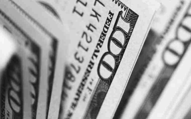 A black and white close-up photo of US currency bills arranged in a fanned-out display, with the focus on the number '100' visible on the top bill. Best £100 Loan
