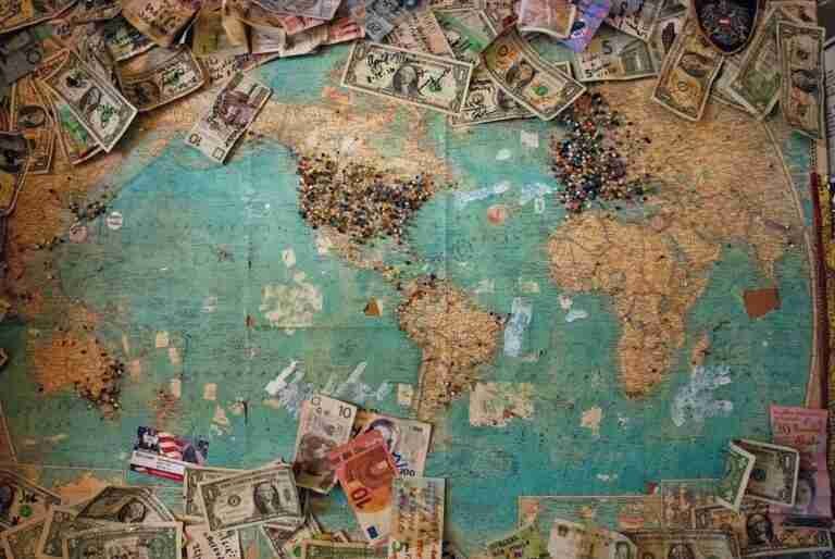 World map on a cork board with various international banknotes and a collection of colorful push pins clustered on different countries. £1000 Loans