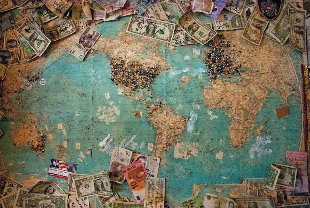 World map on a cork board with various international banknotes and a collection of colorful push pins clustered on different countries. £1000 Loans