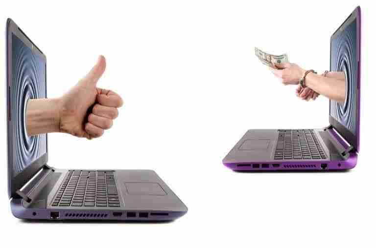 A person giving a thumbs up through one laptop screen to another person offering cash through a second laptop screen, symbolizing an agreement to borrow money now or deal approval.