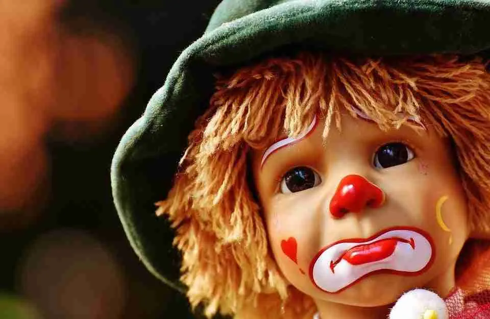 A close-up of a colorful clown doll with a sad expression, featuring a teardrop makeup detail and a heart painted on its cheek, quietly whispering "I need a loan now.
