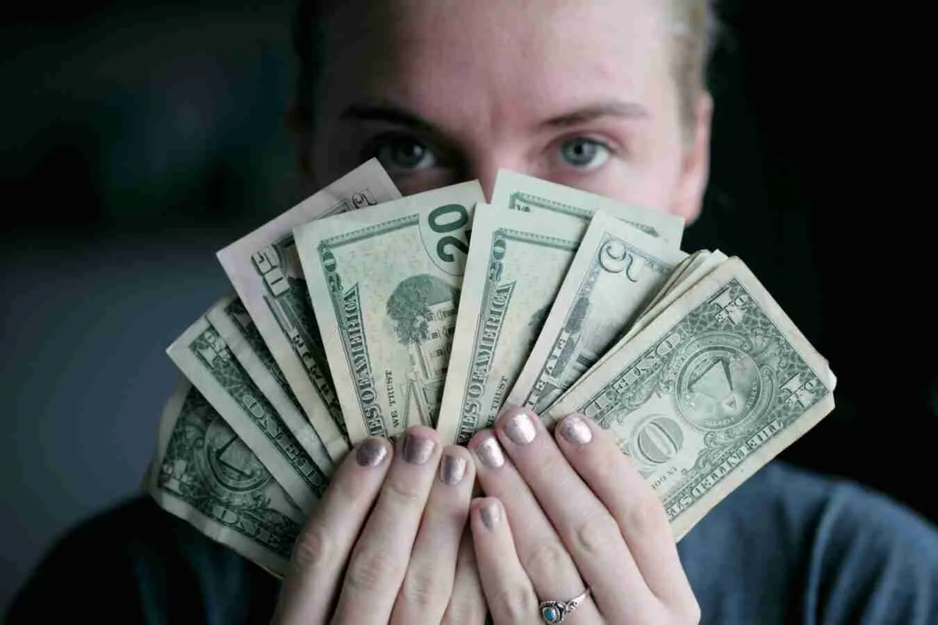 A person holding a fan of various U.S. dollar bills in front of their face, with only their eyes peeking over the top, symbolizing budget finance management.