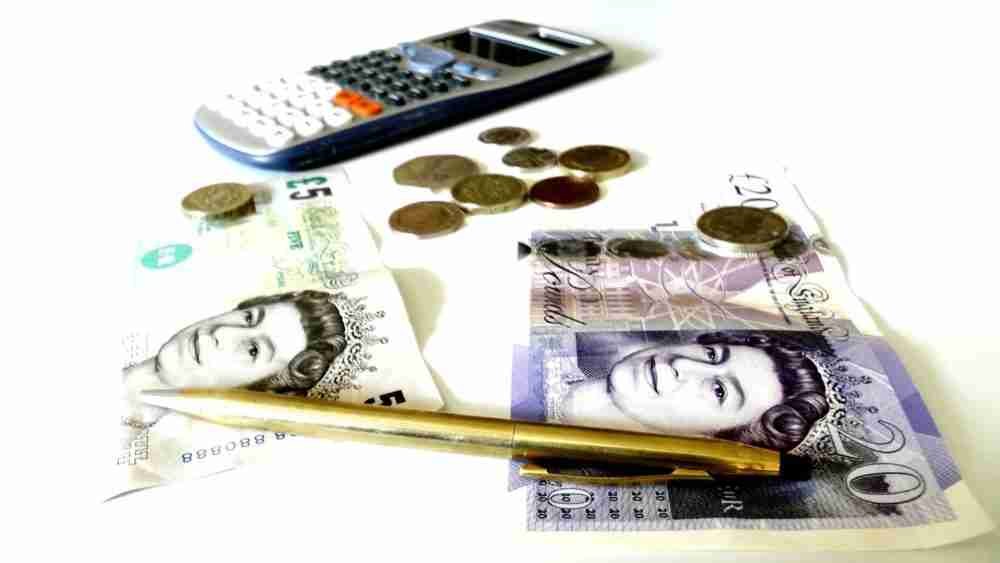 A calculator, a golden pen, and various denominations of British currency, including coins and banknotes, on a white background, suggesting financial calculations or budgeting for poor credit loans.