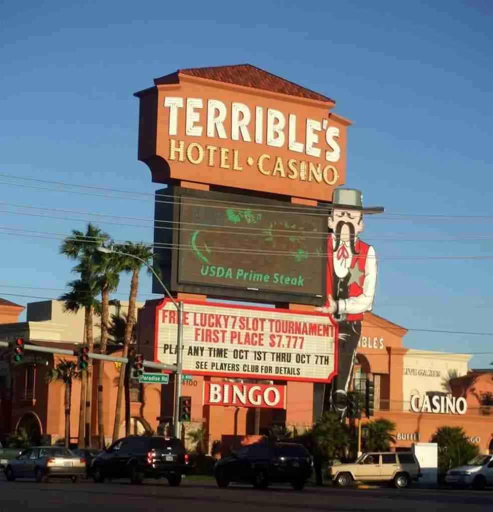 A large, colorful sign for Terrible's Hotel & Casino under a clear blue sky, advertising amenities such as USDA prime steak, slot tournaments, bingo, and loans for terrible credit.