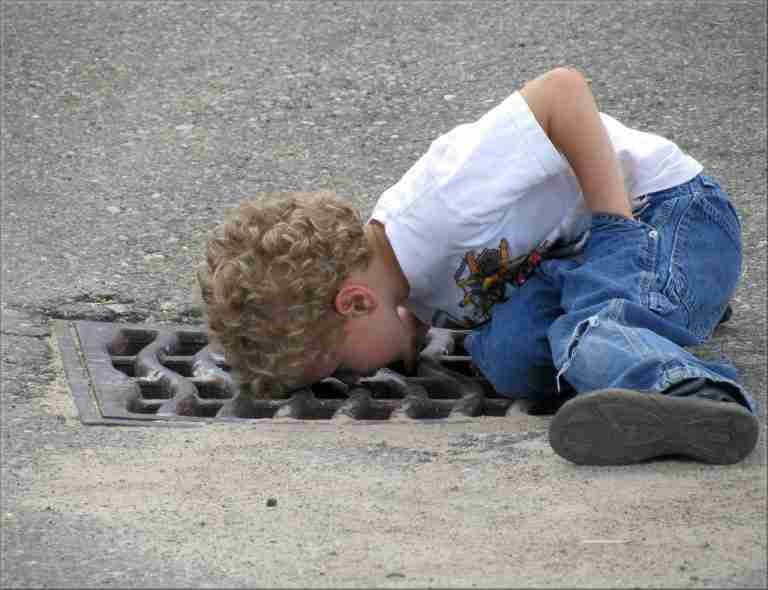 Curious child peering into a storm drain on the street, imagining discovering hidden cash advance loans.