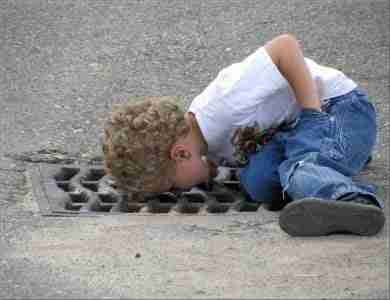 Curious child peering into a storm drain on the street, imagining discovering hidden cash advance loans.